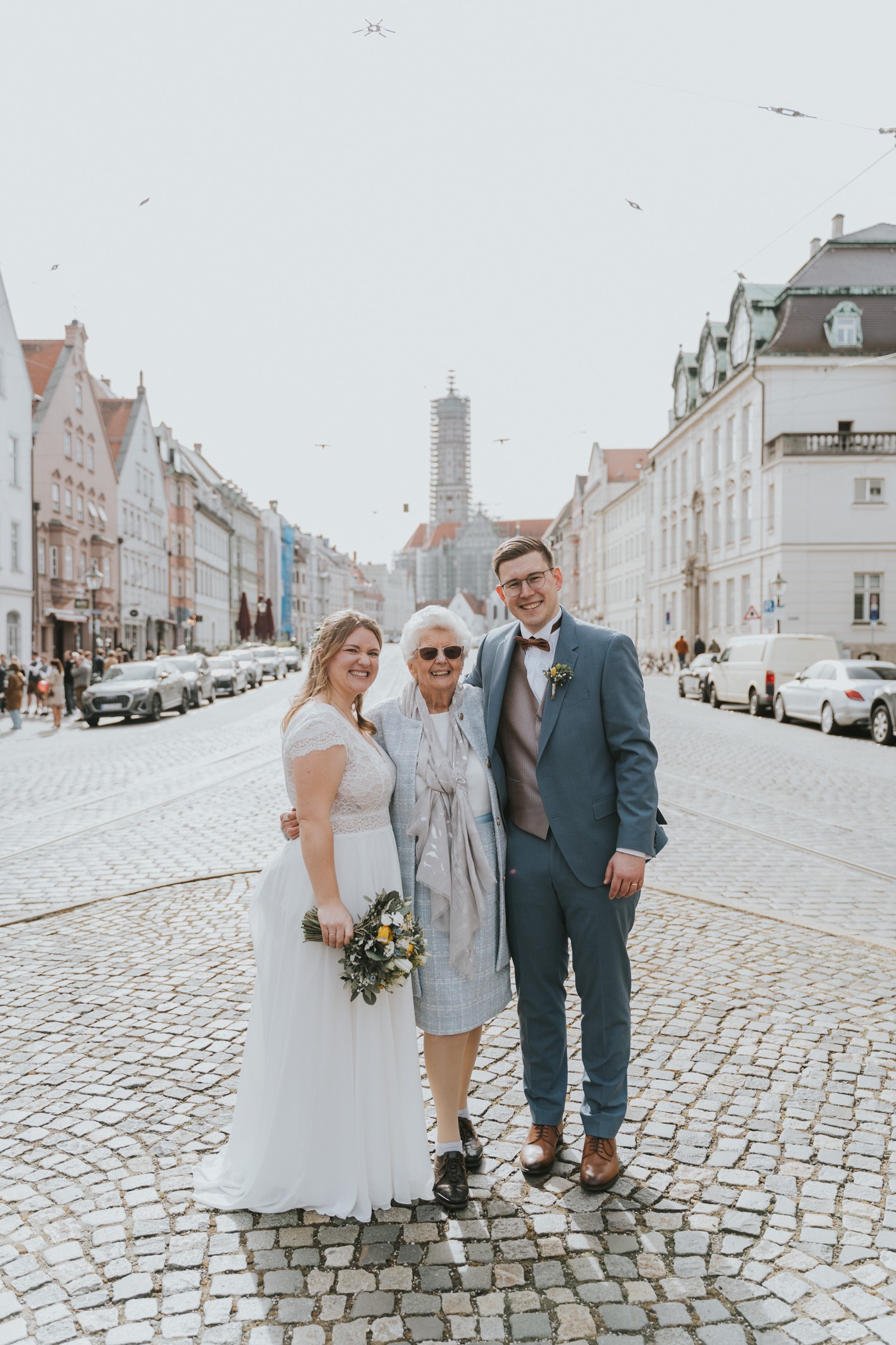 Fröhlicher Moment: Brautpaar und Großmutter lachen – Authentische Hochzeitsfotografie in Augsburg in der Maxstraße